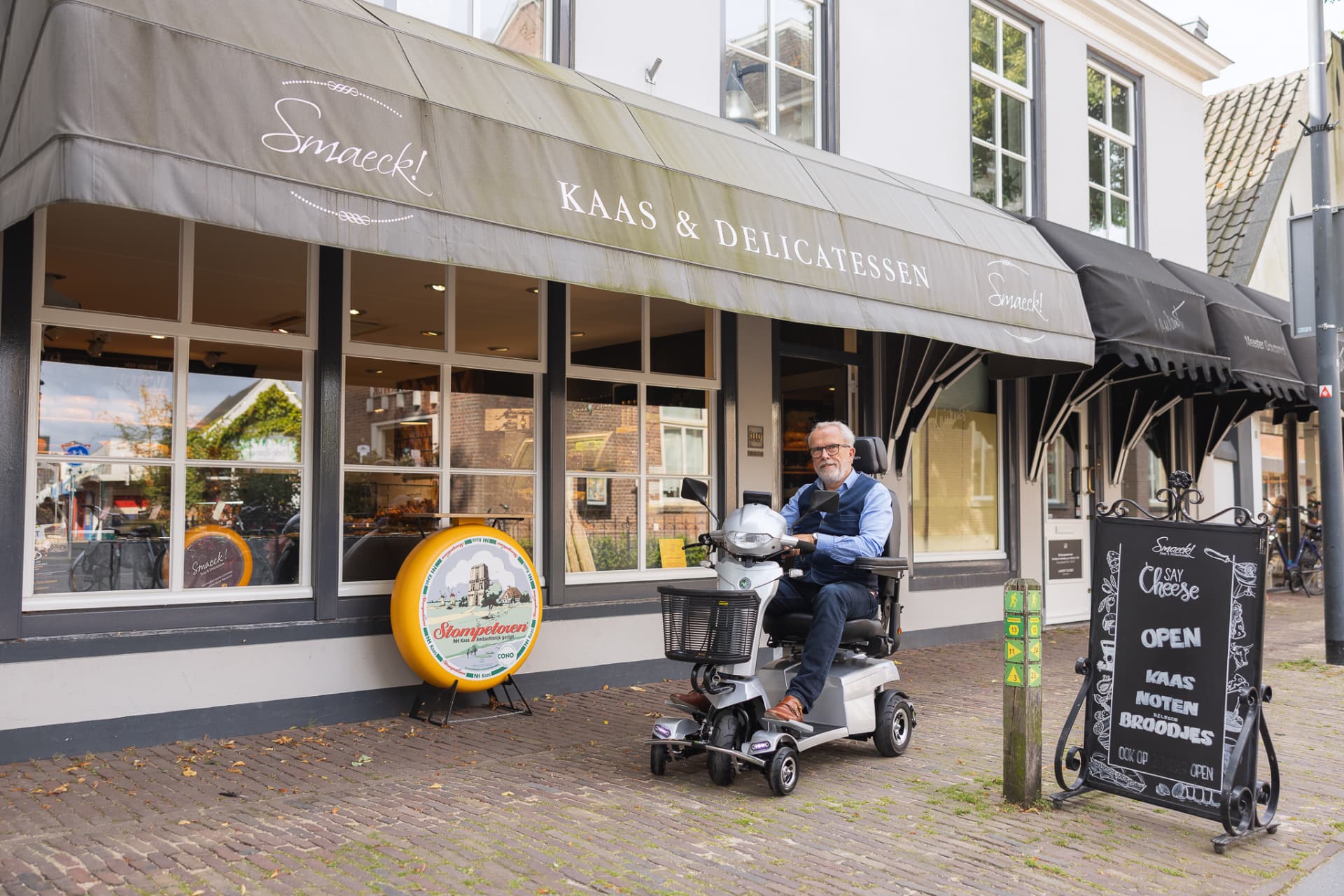Een man op een scootmobiel staat voor een winkel in een dorpsstraat.