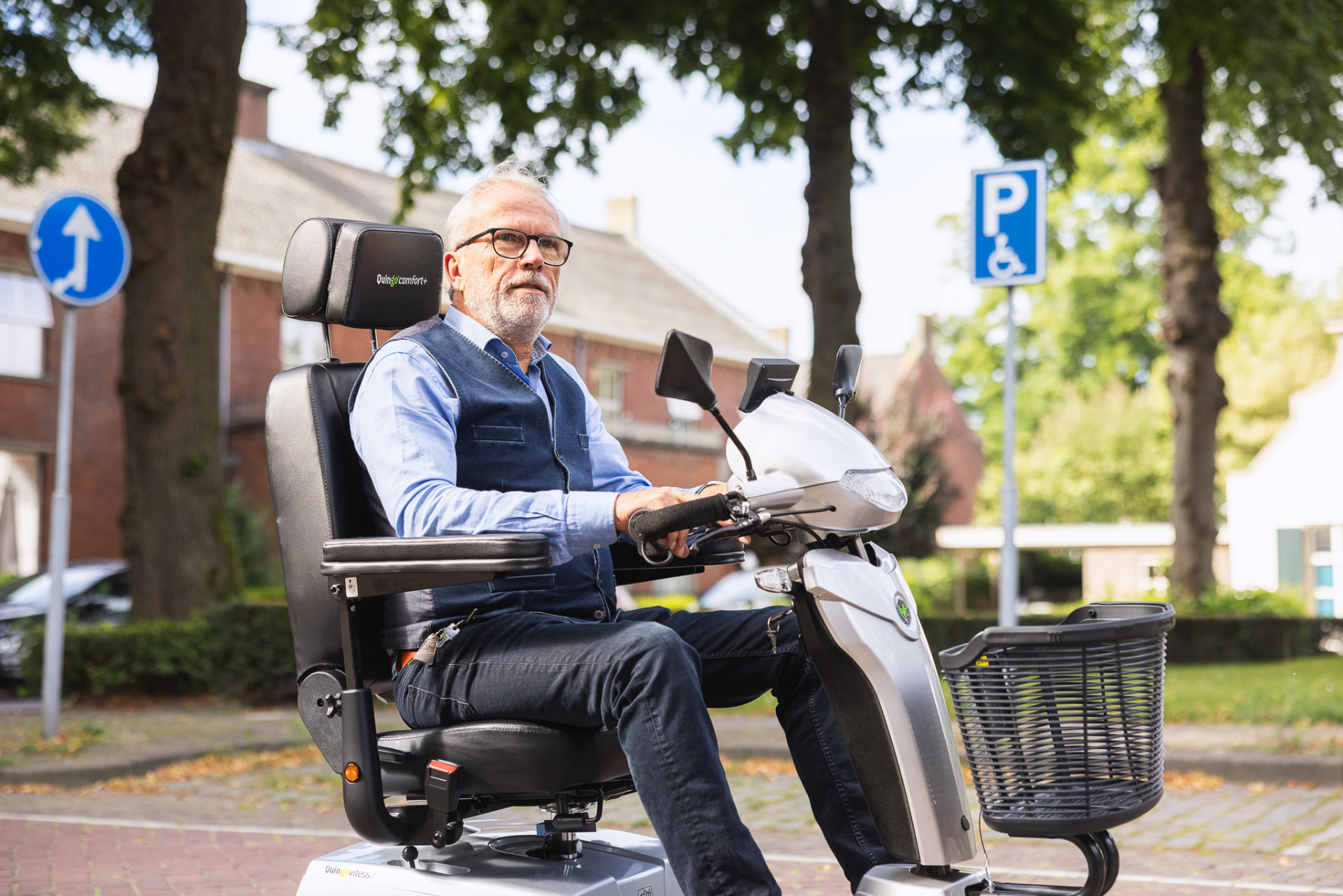 Een man op een witte scootmobiel bij een gehandicaptenparkeerplaats.