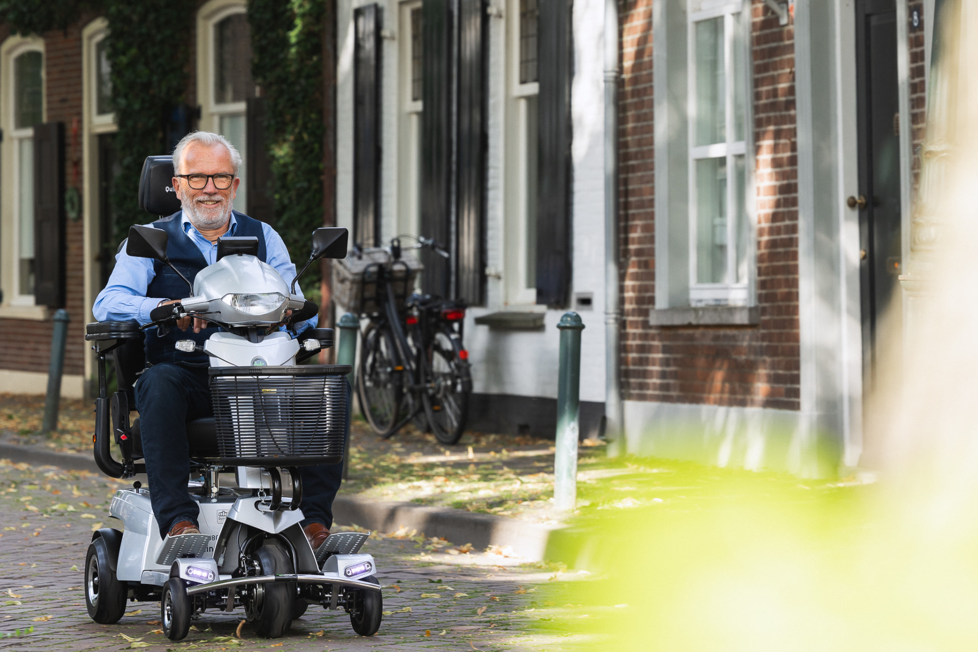 Een man rijdt lachend op een witte scootmobiel door een stadsstraat.