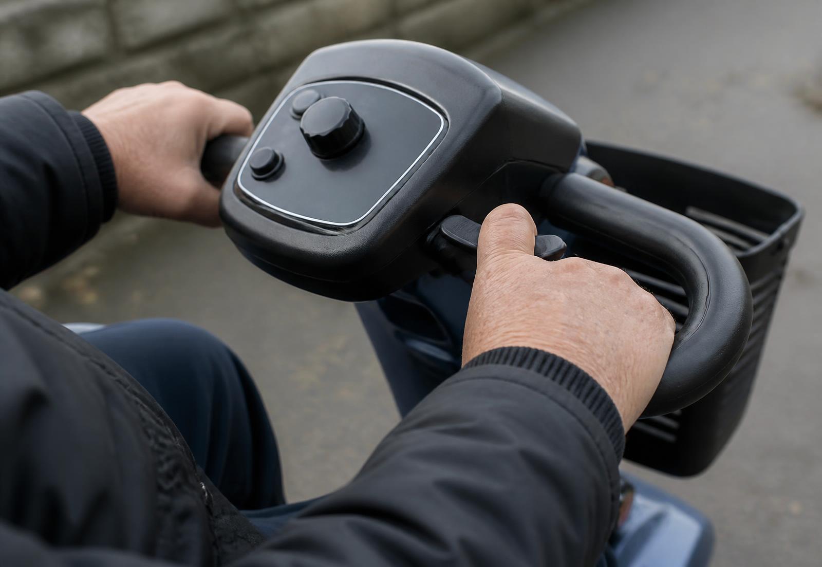 Twee handen bedienen het stuur en de gaspaddle van een scootmobiel.