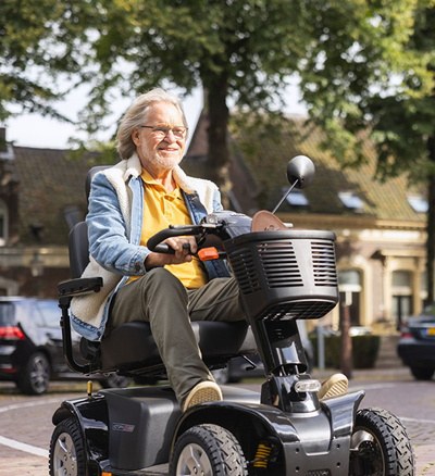 Een scootmobielgebruiker rijdt over een plein in een dorpskern.